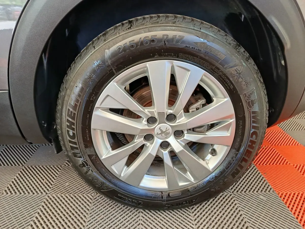 Gros plan sur la roue avant droite d’un Peugeot 3008 gris foncé, avec jante alliage et pneu Michelin visible.