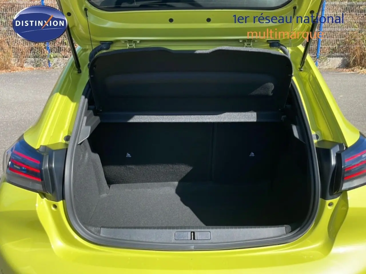 Coffre ouvert vu de l'arrière d'une Peugeot 208 Hybrid 110ch Allure en jaune Agueda métal, montrant l'espace de chargement vide.