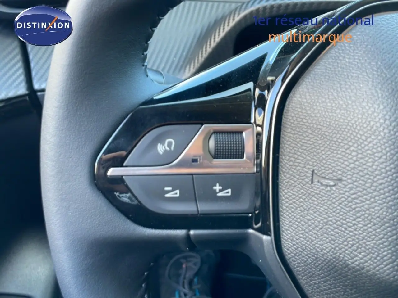 Gros plan sur les commandes de volume au volant d'une Peugeot 208 Hybrid 110ch Allure, intérieur noir.