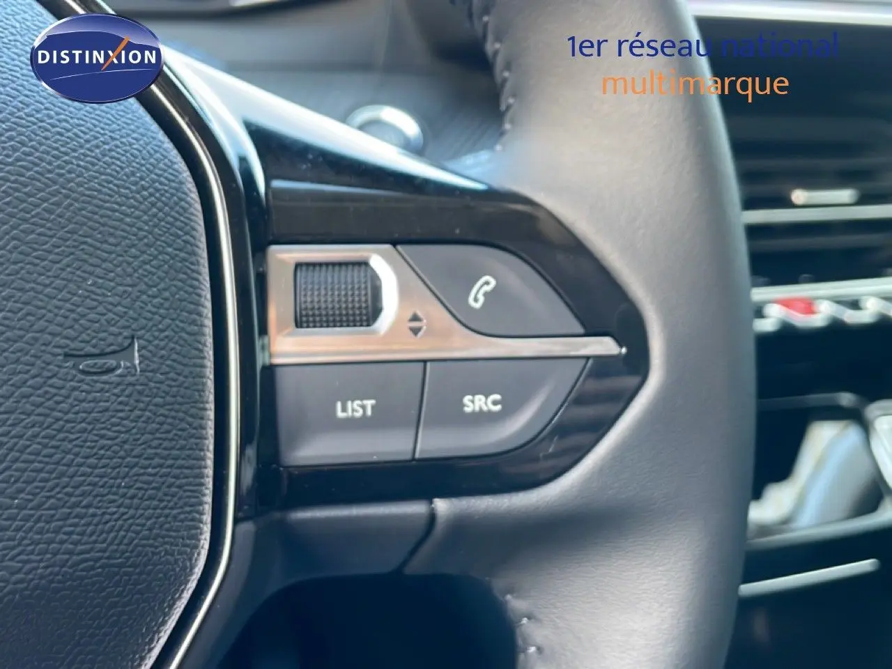 Détail du côté gauche du volant en cuir noir d'une Peugeot 208 Hybrid jaune, avec commandes audio intégrées.
