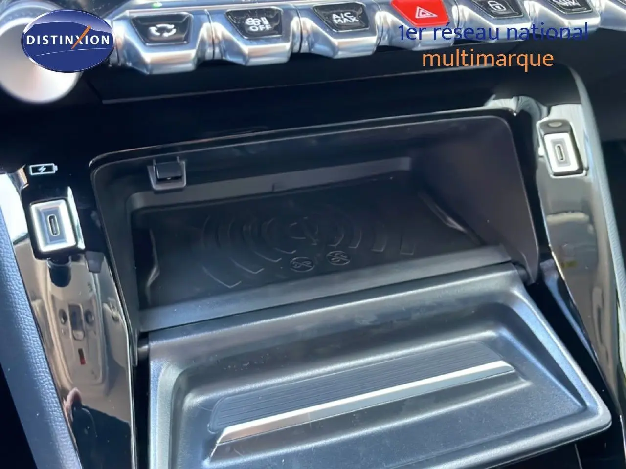 Gros plan sur la console centrale noire brillante de la Peugeot 208 Hybrid 110ch, montrant le chargeur sans fil et les commandes.