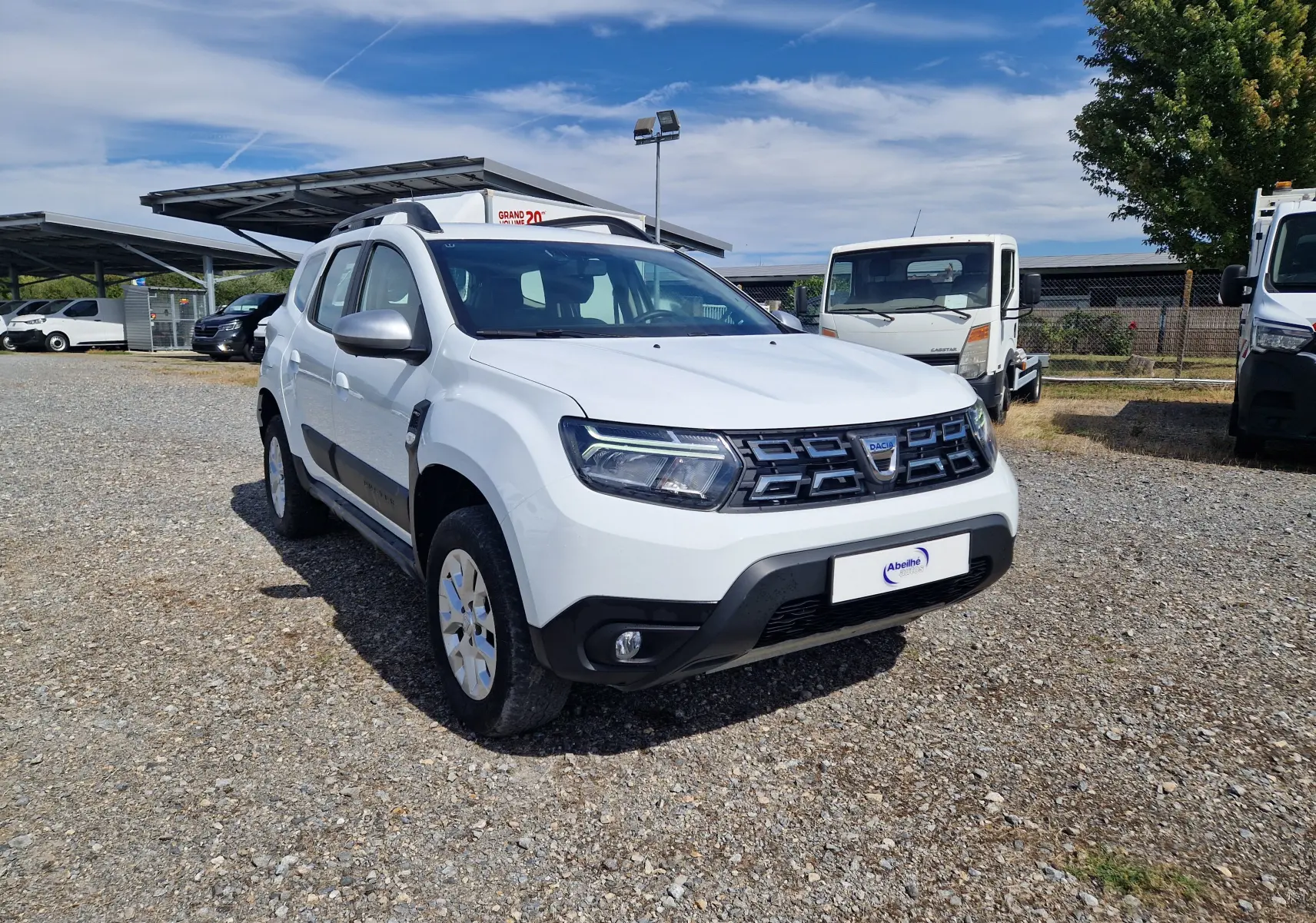 Dacia Duster blanc vue 3/4 avant droit, avec calandre noire et protections noires sur les bas de caisse.