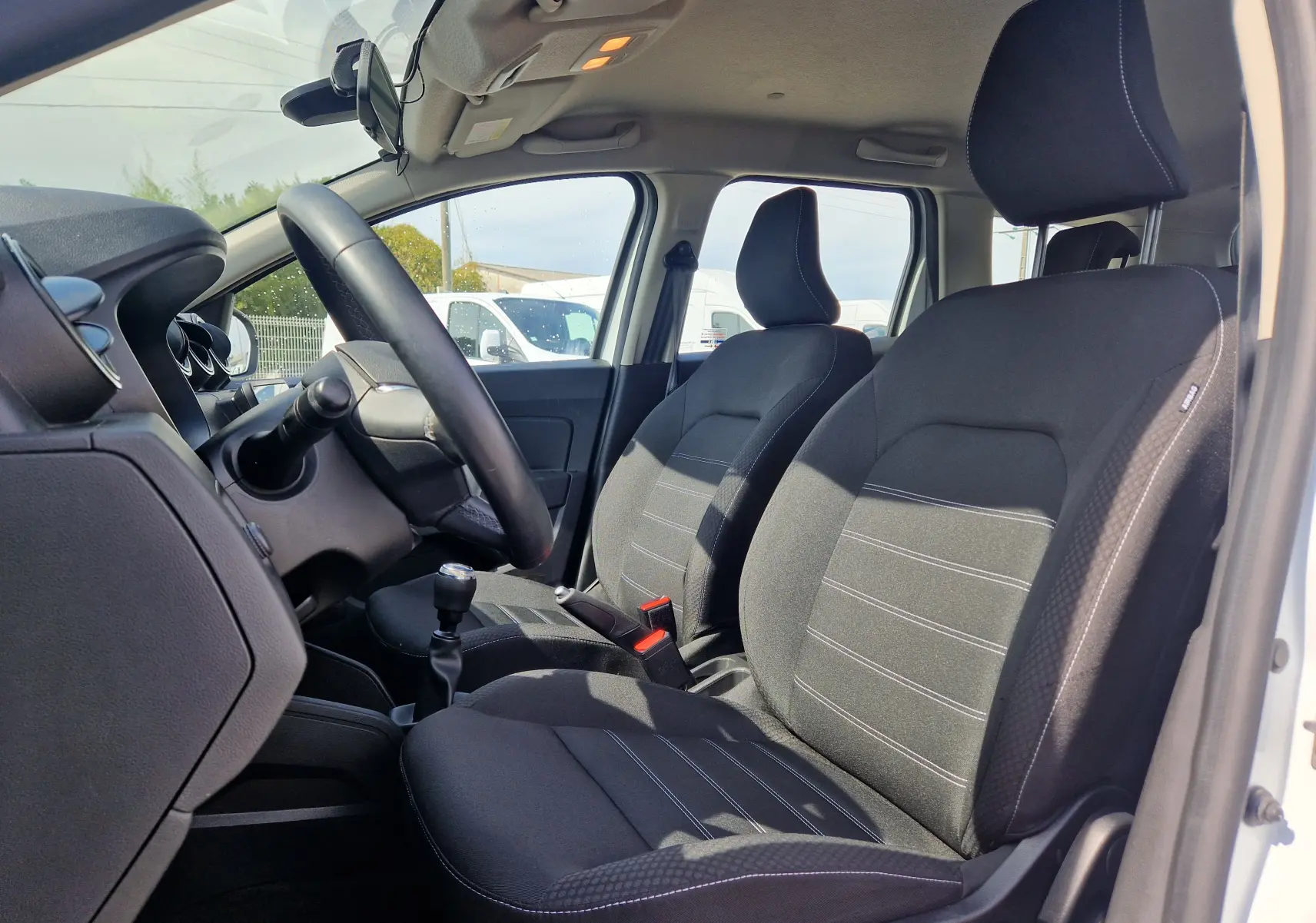 Vue intérieure côté conducteur du Dacia Duster blanc 2023, sièges noirs avec surpiqûres blanches et volant visible.