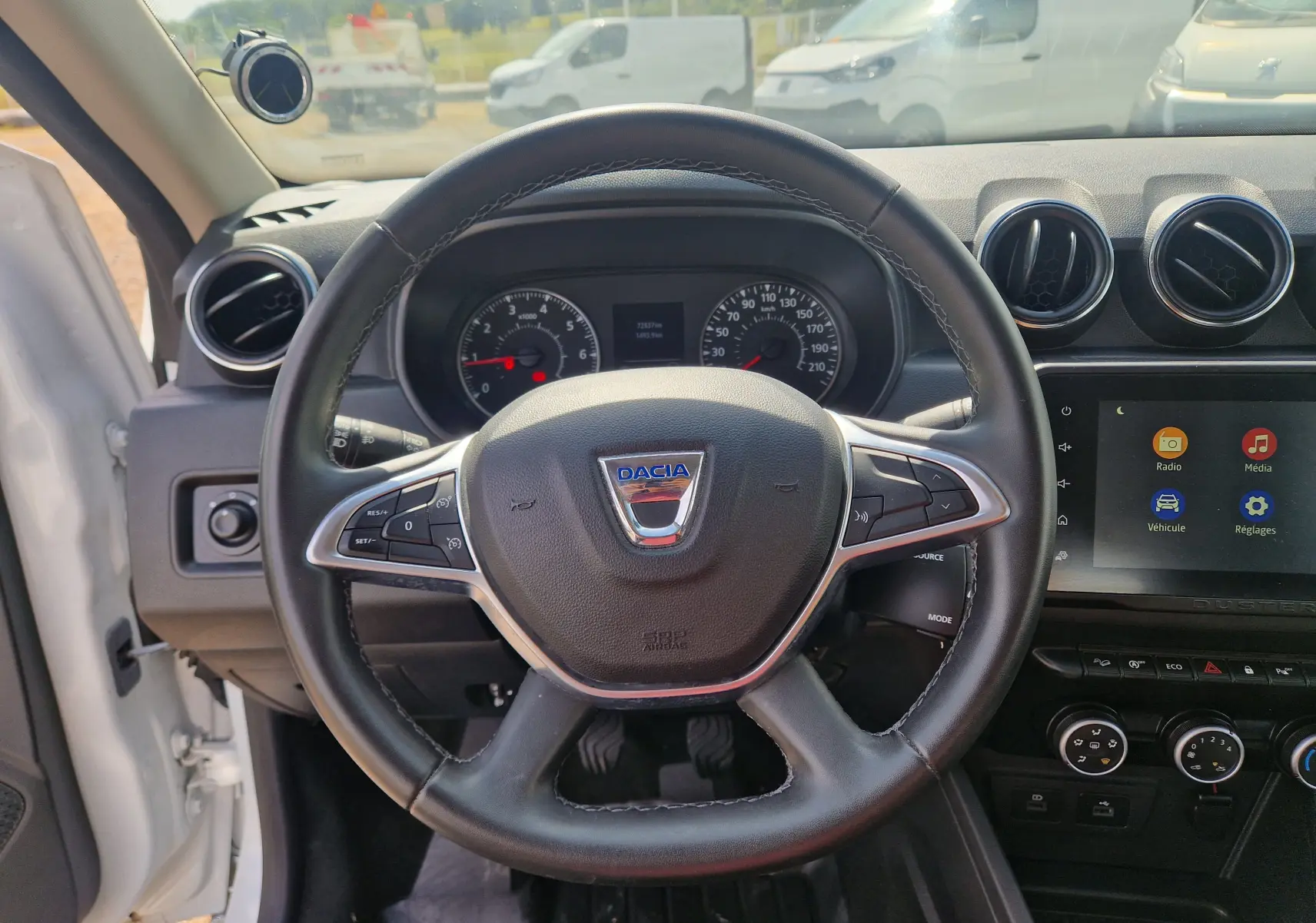 Vue intérieure centrée sur le volant du Dacia Duster blanc 2023, avec tableau de bord et écran tactile visibles.