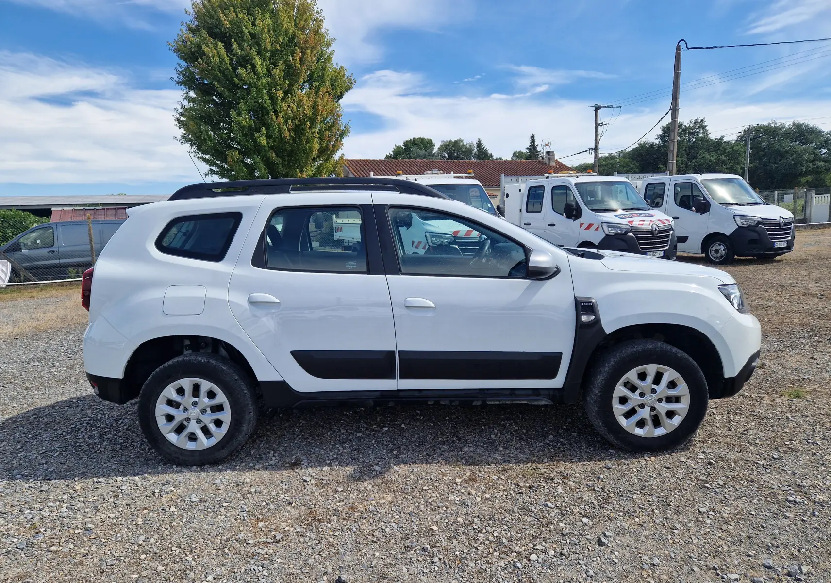 Vue de profil côté gauche d'un Dacia Duster blanc 4x4 2023 avec protections noires et jantes alliage 16 pouces.