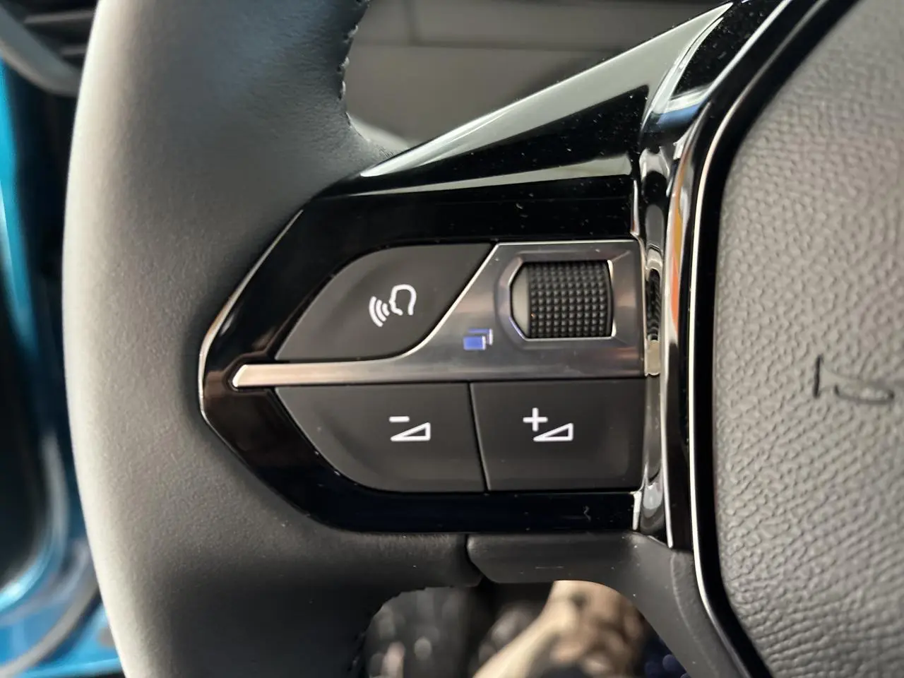 Gros plan sur les commandes noires du volant cuir du Peugeot 2008 bleu, avec bouton volume et assistant vocal.