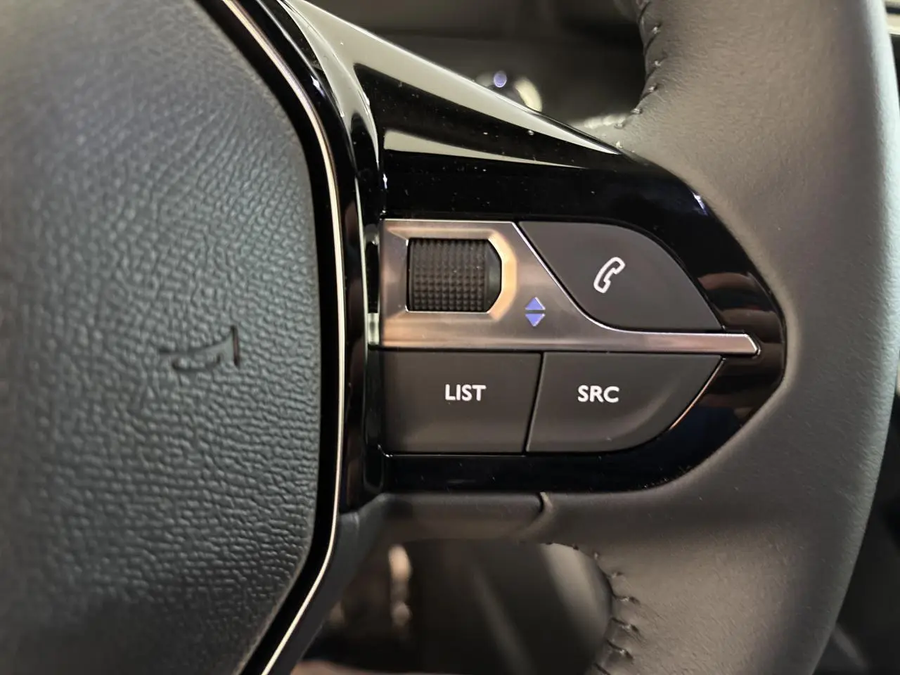 Gros plan sur les commandes multimédia noires et chrome intégrées au volant cuir gris du Peugeot 2008 hybride.