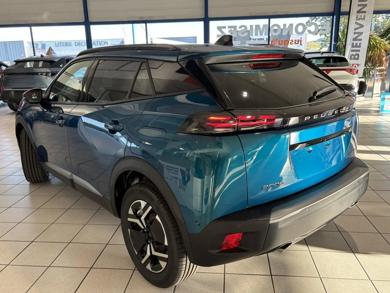 Peugeot 2008 bleu 3/4 arrière droit en showroom, feux LED et jantes alliage bi-ton visibles.