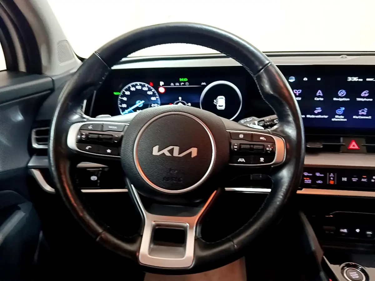 Vue intérieure centrée sur le volant cuir KIA avec tableau de bord numérique et écran tactile du Sportage blanc 2022.