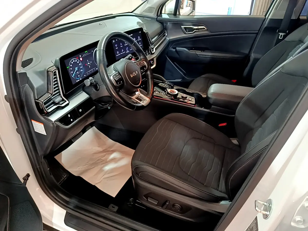 Intérieur avant du Kia Sportage blanc 2022, vue côté conducteur, avec tableau de bord digital et sièges noirs.