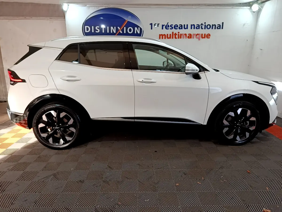 Profil droit d'un KIA SPORTAGE blanc 2022 avec jantes noires et détails noirs contrastants sous un éclairage intérieur.