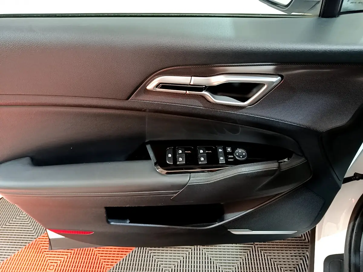 Gros plan sur la porte avant gauche blanche du Kia Sportage 2022 avec commandes électriques et poignée argentée.