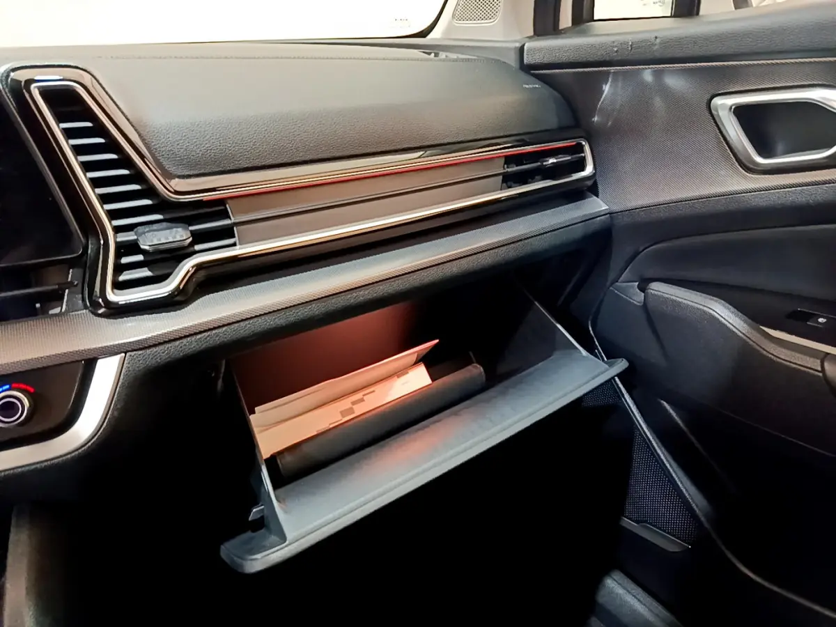 Vue intérieure côté passager du tableau de bord noir du Kia Sportage 2022 avec boîte à gants ouverte contenant des documents.