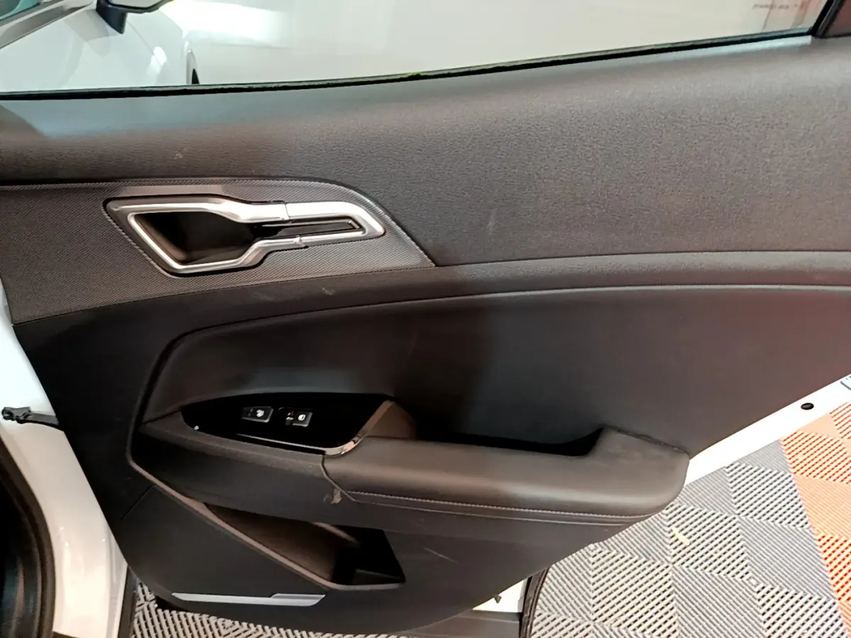 Vue intérieure de la porte avant gauche du KIA SPORTAGE blanc, avec poignée argentée et commandes de vitres.