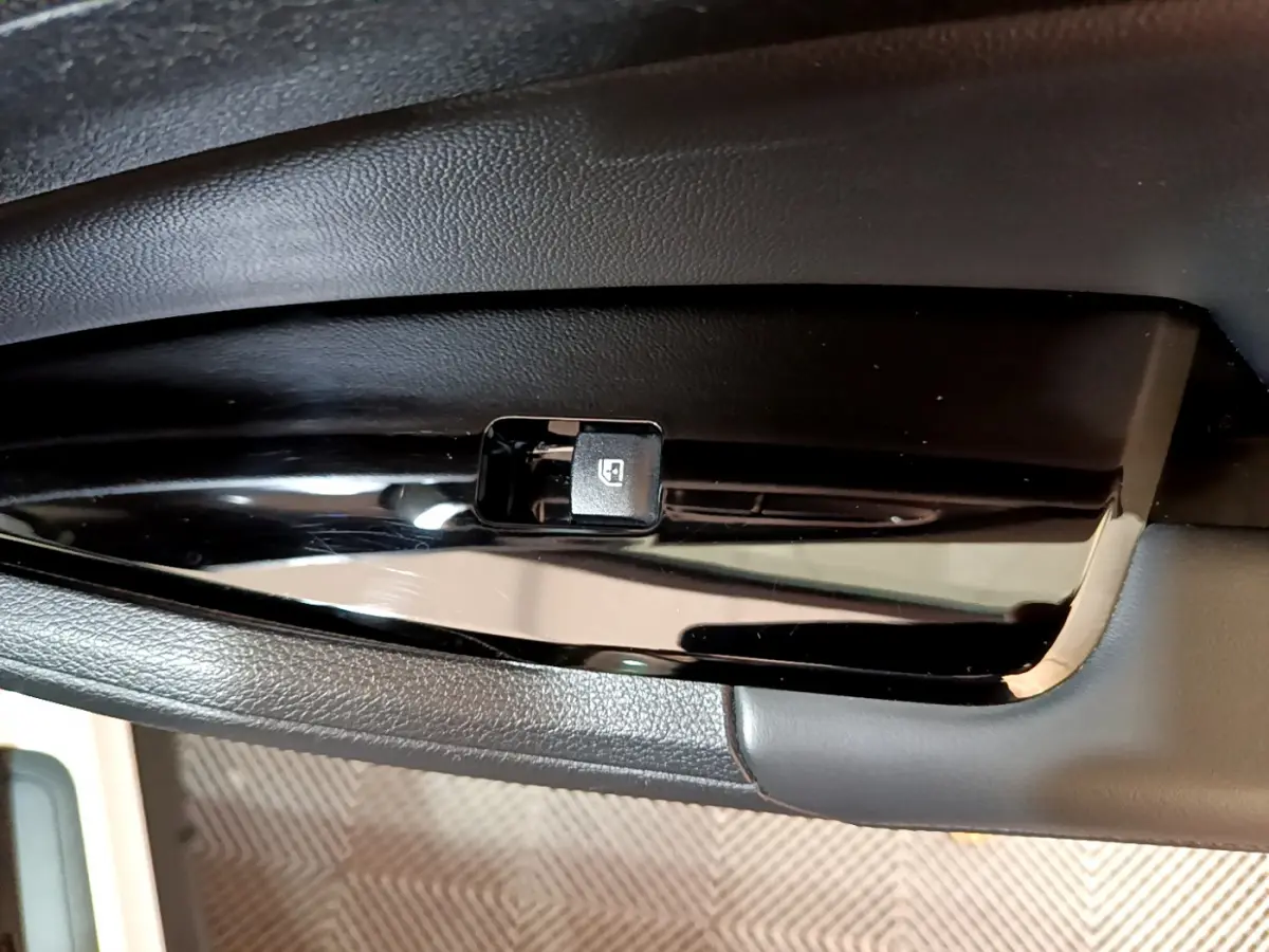 Bouton de commande de lève-vitre électrique noir sur panneau de porte intérieur du Kia Sportage blanc, vue rapprochée.