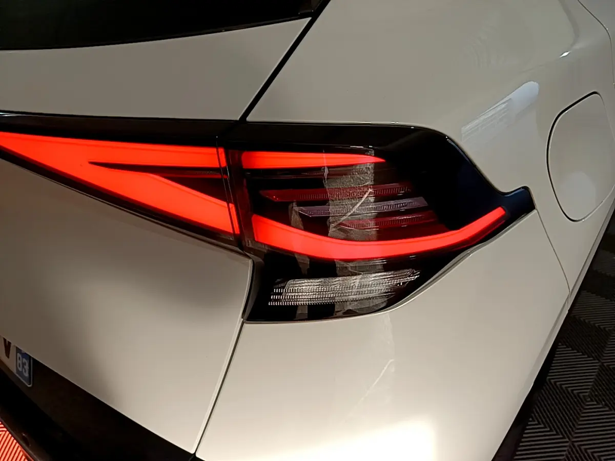 Gros plan sur le feu arrière droit rouge vif du KIA SPORTAGE blanc hybride rechargeable 2022, détail du coffre et trappe à carburant.