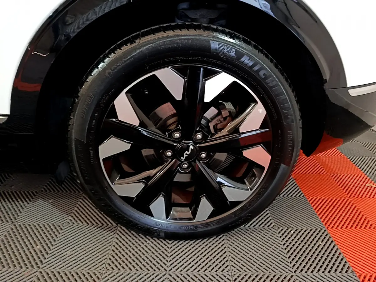 Gros plan sur la roue avant droite du Kia Sportage blanc 2022 avec jante noire et argentée au design moderne.