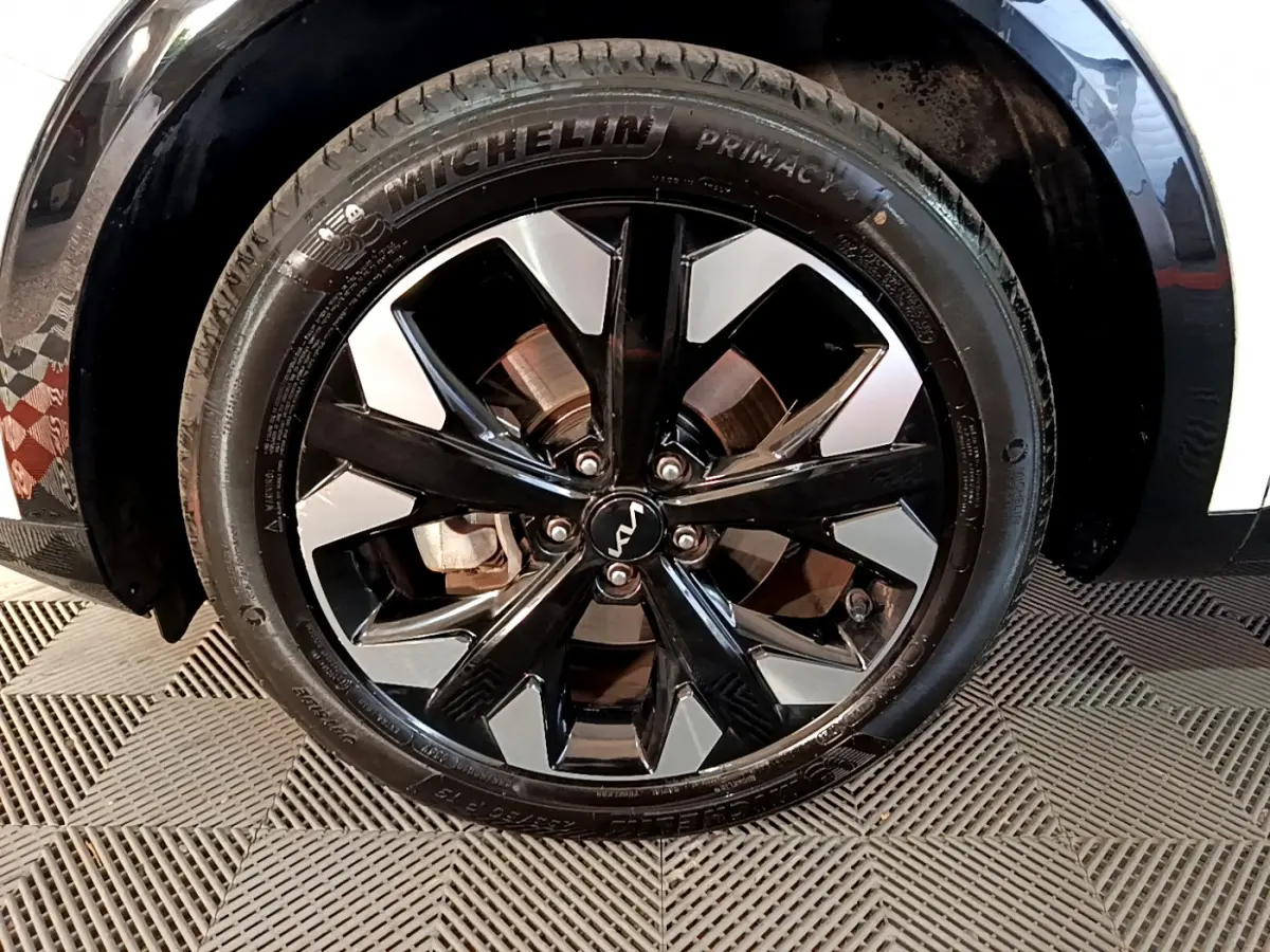 Gros plan sur la roue avant droite du KIA SPORTAGE blanc, jante alliage noir et argent avec logo KIA central.