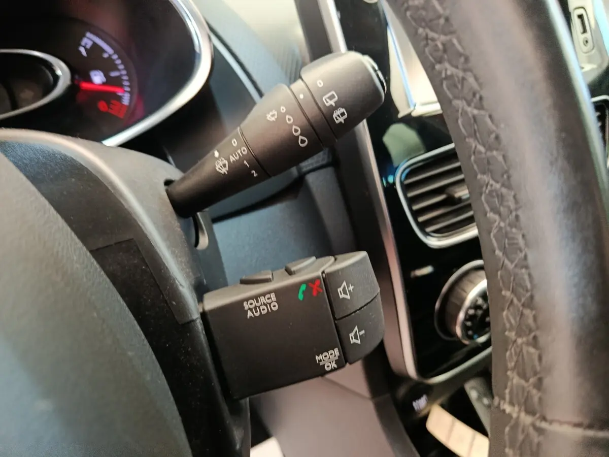 Gros plan sur la commande audio au volant et la manette d’essuie-glace d’une Renault Clio Intens rouge, intérieur noir.