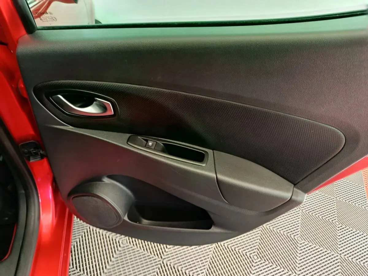 Gros plan sur la porte arrière gauche rouge de la Renault Clio Intens avec habillage noir et commande de vitre électrique.