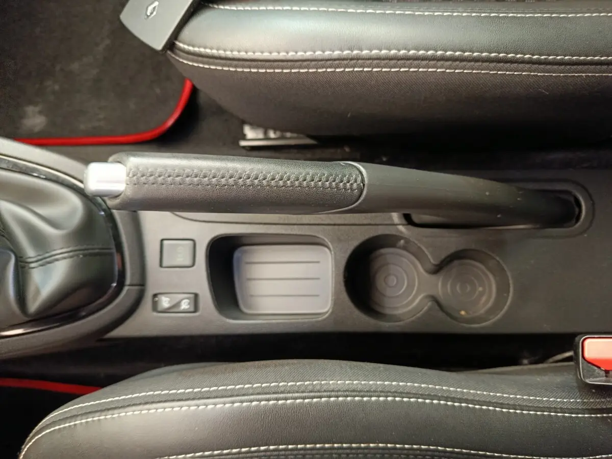 Vue plongeante sur la console centrale noire de la Renault Clio Intens avec frein à main manuel et porte-gobelets.