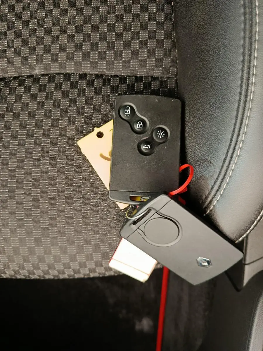 Gros plan sur les clés noires Renault posées sur un siège tissu noir à motifs, avec coutures blanches visibles.
