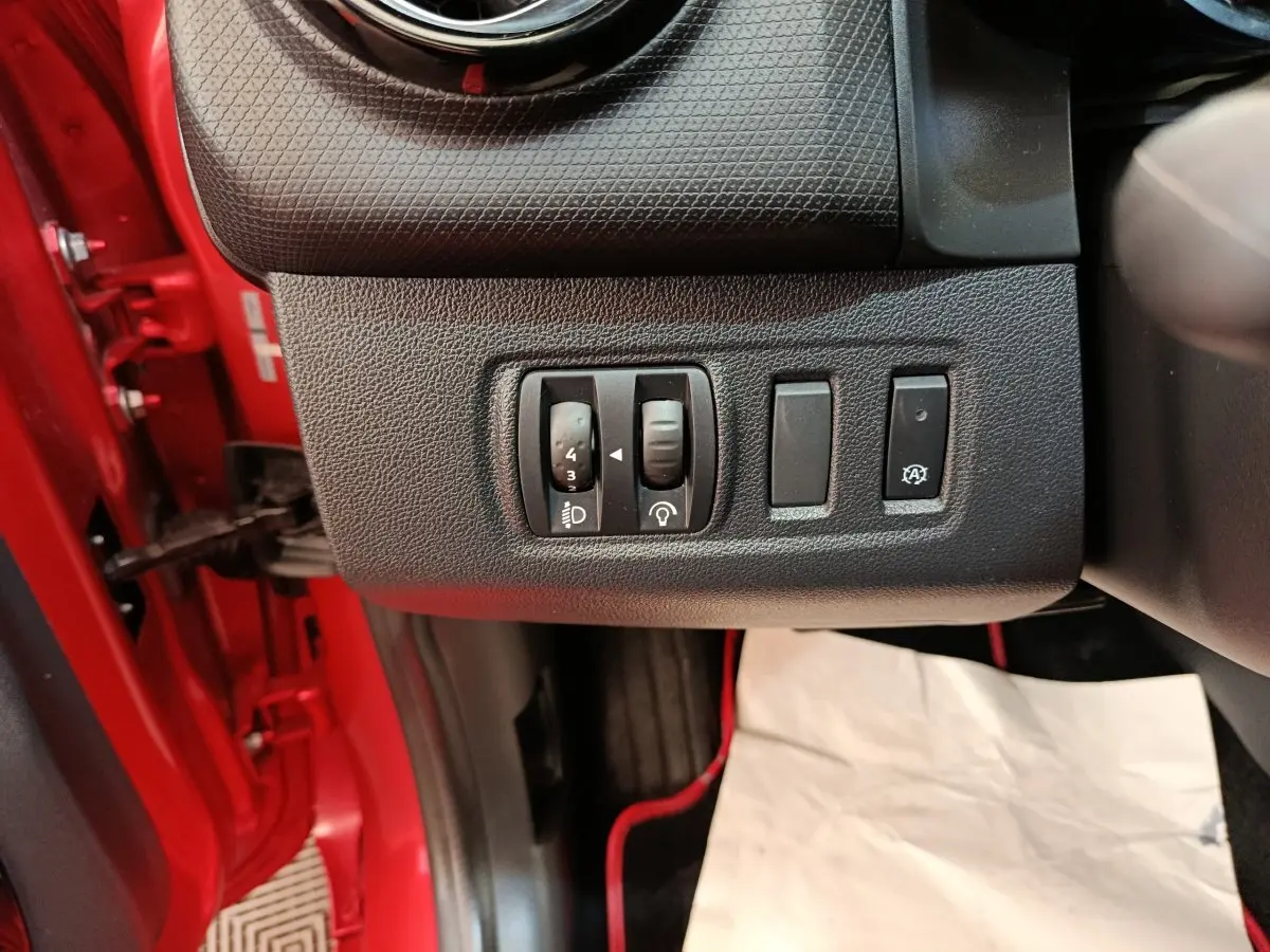 Vue intérieure côté conducteur de la Renault Clio Intens rouge, avec commandes de réglage des phares et fonction arrêt/start.