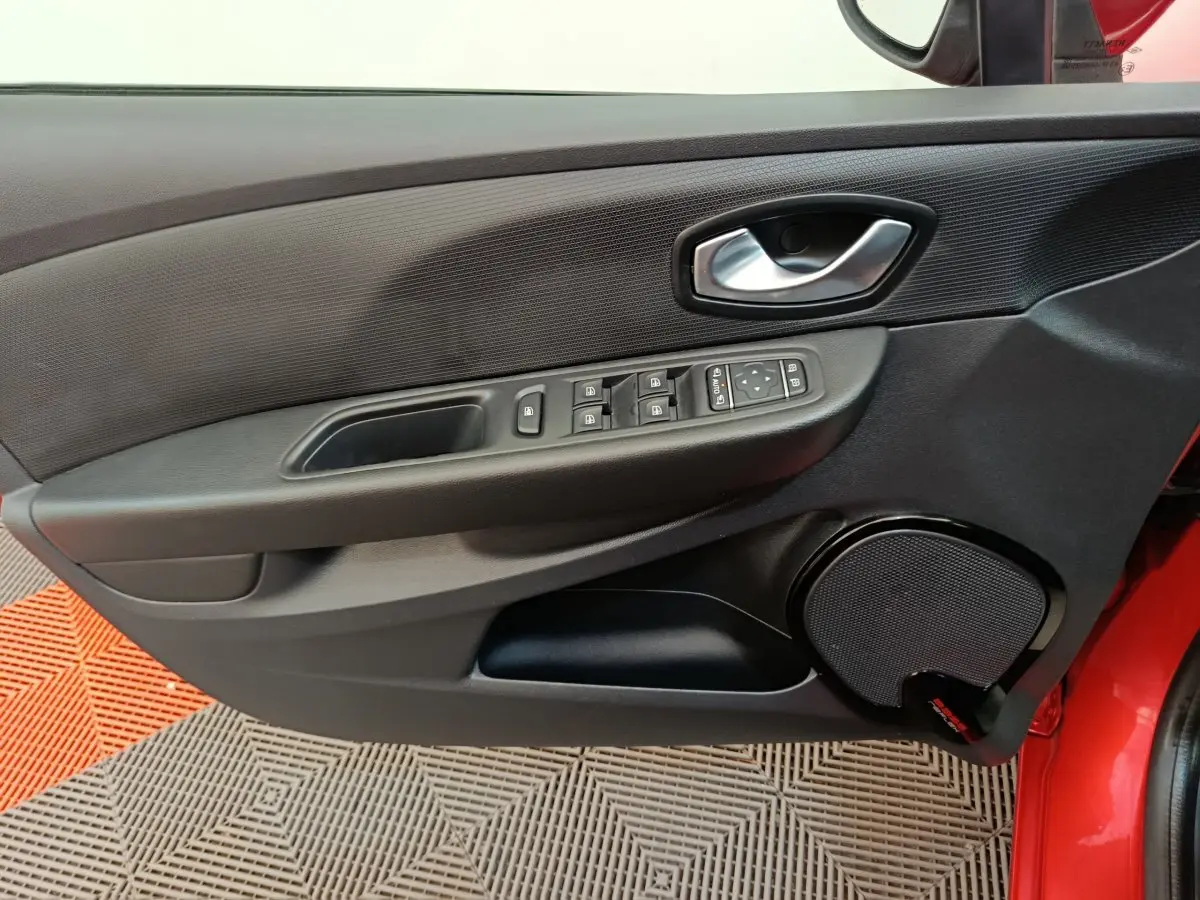 Vue rapprochée de la porte avant gauche rouge de la Renault Clio Intens avec commandes de vitres et haut-parleur intégré.