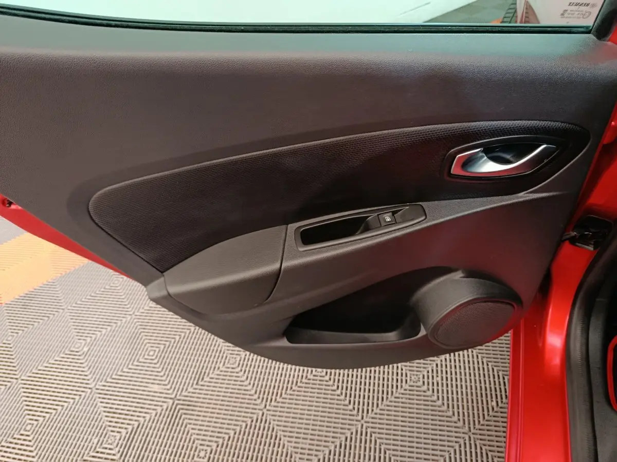 Vue rapprochée de la porte avant gauche rouge de la Renault Clio Intens 2018 avec commande de vitre et poignée intérieure.