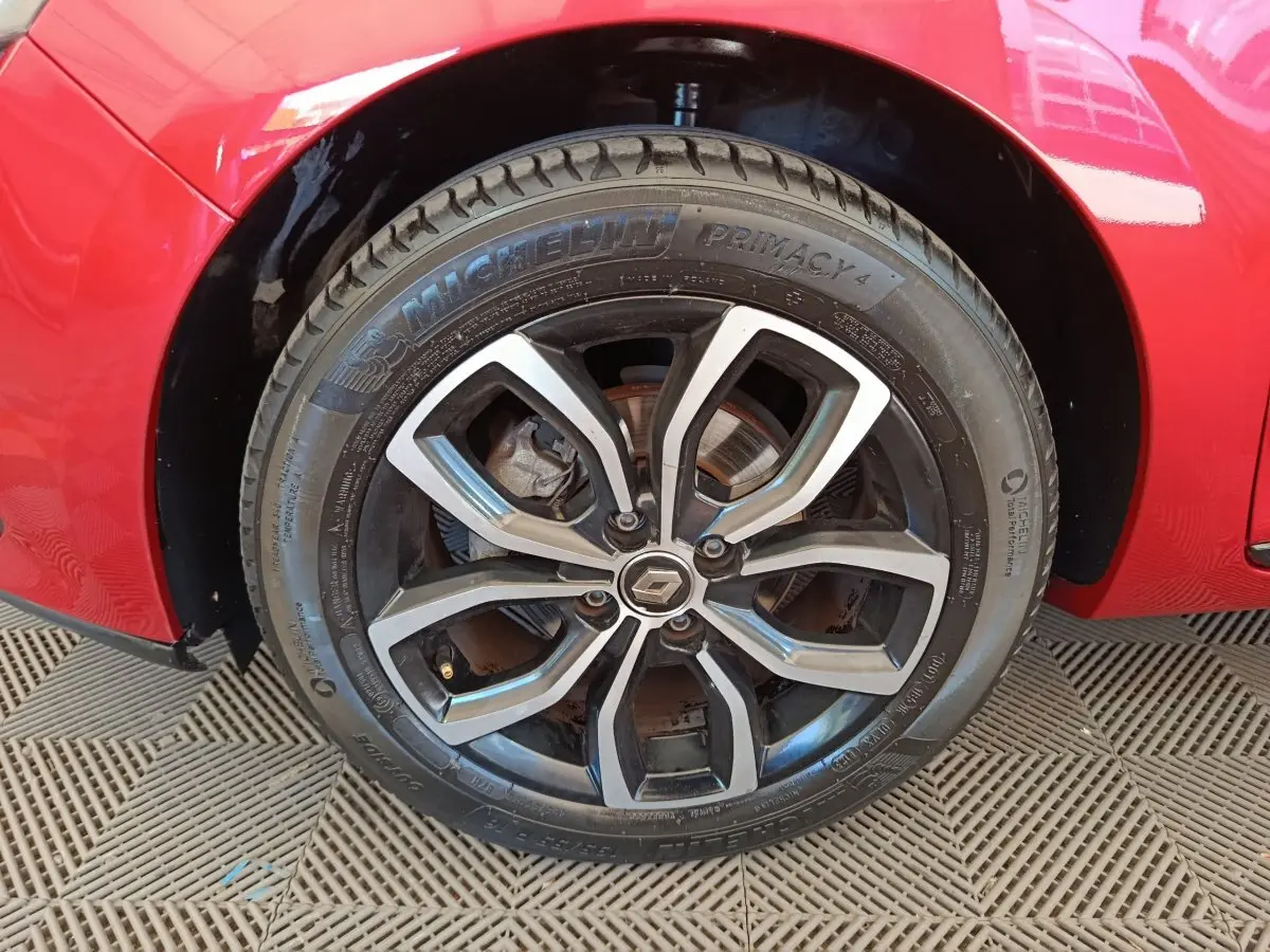 Gros plan sur la roue avant gauche d'une Renault Clio rouge, jante alliage au design moderne et pneu Michelin.