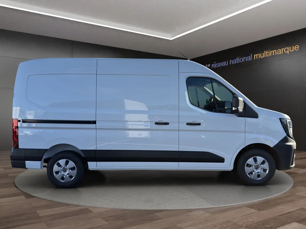Profil droit d’un utilitaire Renault Master blanc avec bande noire et jantes argentées, en intérieur showroom.