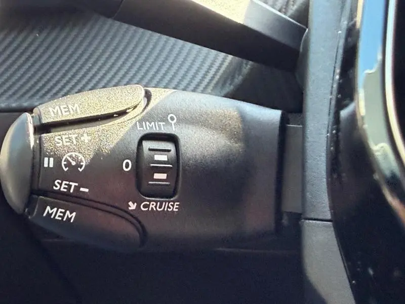 Gros plan sur la commande de régulateur de vitesse noire dans l'habitacle d'une Peugeot 208 blanche.
