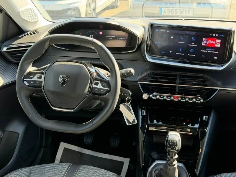 Vue intérieure centrée sur le volant et la console centrale d'une Peugeot 208 blanche avec boîte manuelle et écran tactile.
