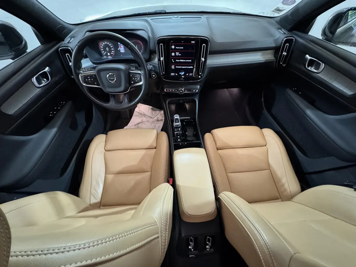 Vue intérieure avant du Volvo XC40 Recharge T5 avec sièges cuir beige et tableau de bord noir moderne à écran tactile central.