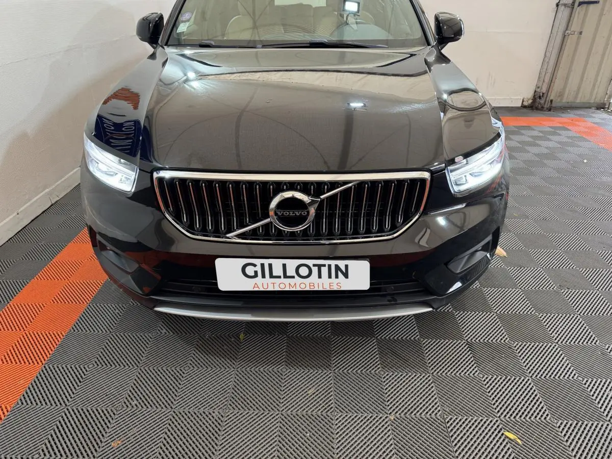 Vue avant rapprochée d’un Volvo XC40 noir avec calandre chromée et phares LED allumés dans un garage.