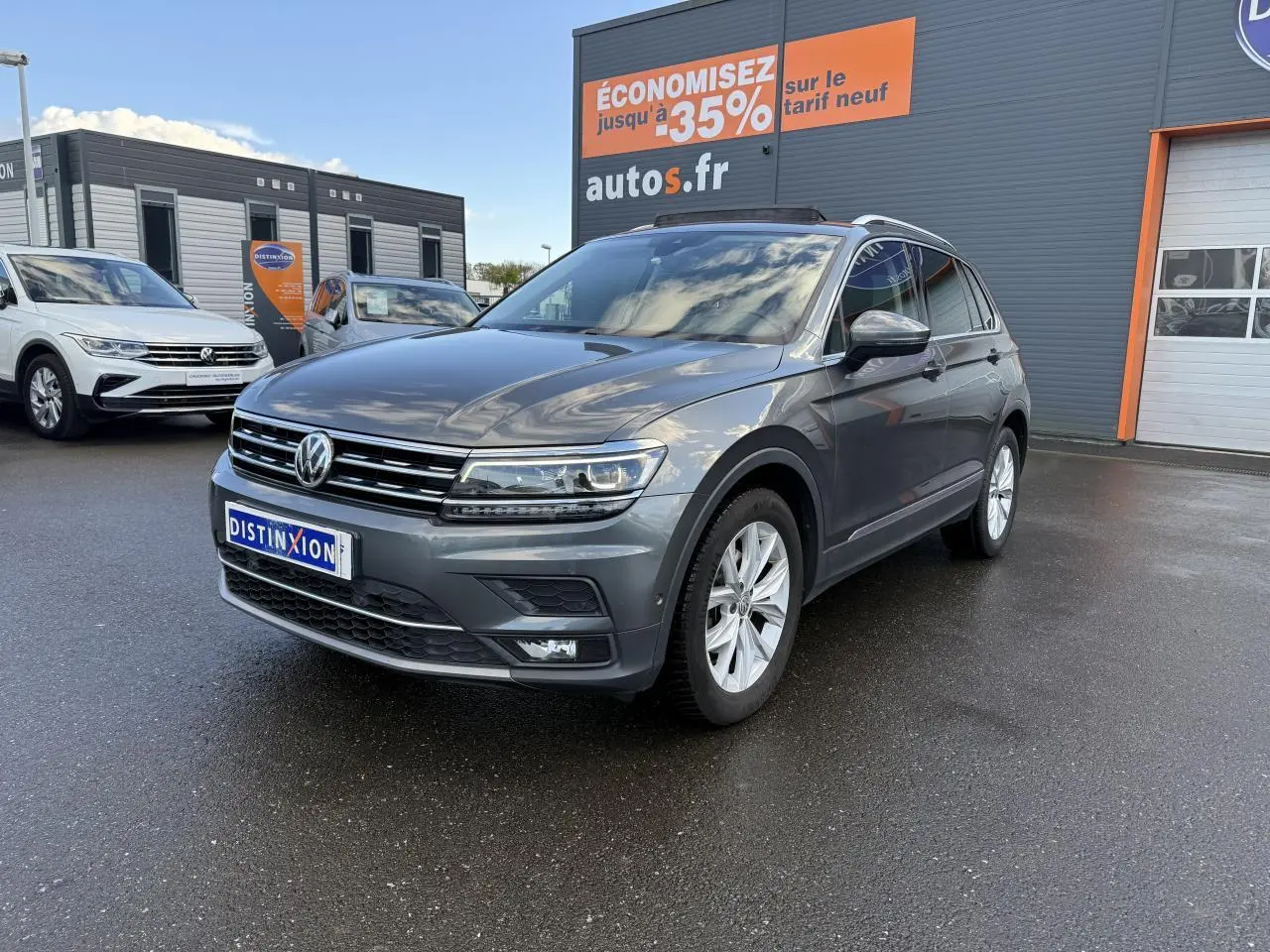 Volkswagen Tiguan gris Indium métallisé vu en 3/4 avant droit sur parking devant un bâtiment commercial.