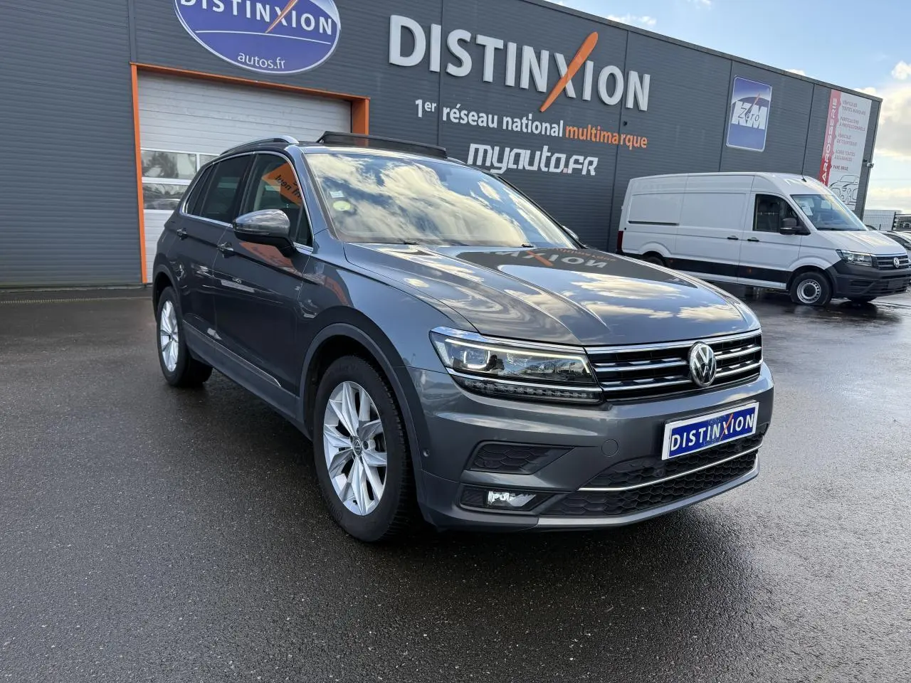 Volkswagen Tiguan gris Indium métallisé vu en 3/4 avant droit sur parking devant un bâtiment Distinxion.