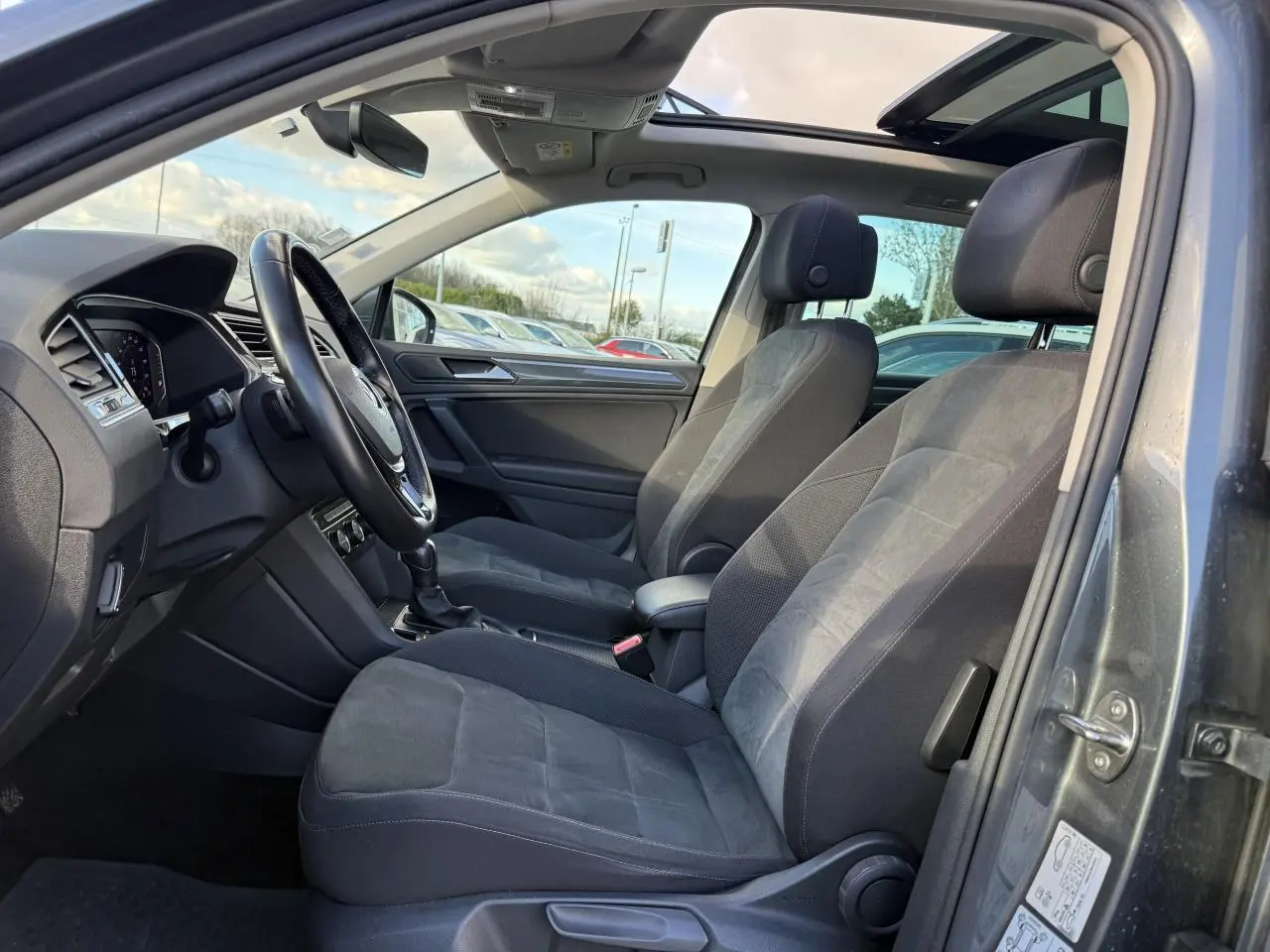 Vue intérieure côté conducteur du Volkswagen Tiguan gris Indium, sièges sport et toit ouvrant panoramique visibles
