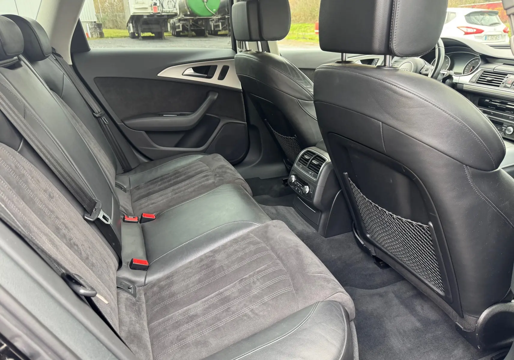 Vue intérieure arrière côté gauche d'une Audi A6 Avant 2015 noire avec sièges en cuir et alcantara, climatisation arrière visible.