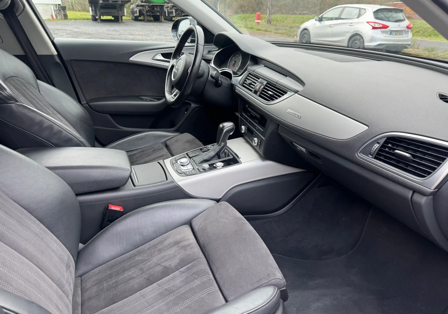 Vue intérieure côté conducteur de l'Audi A6 Avant 2015, montrant les sièges cuir et alcantara gris et la console centrale argentée.