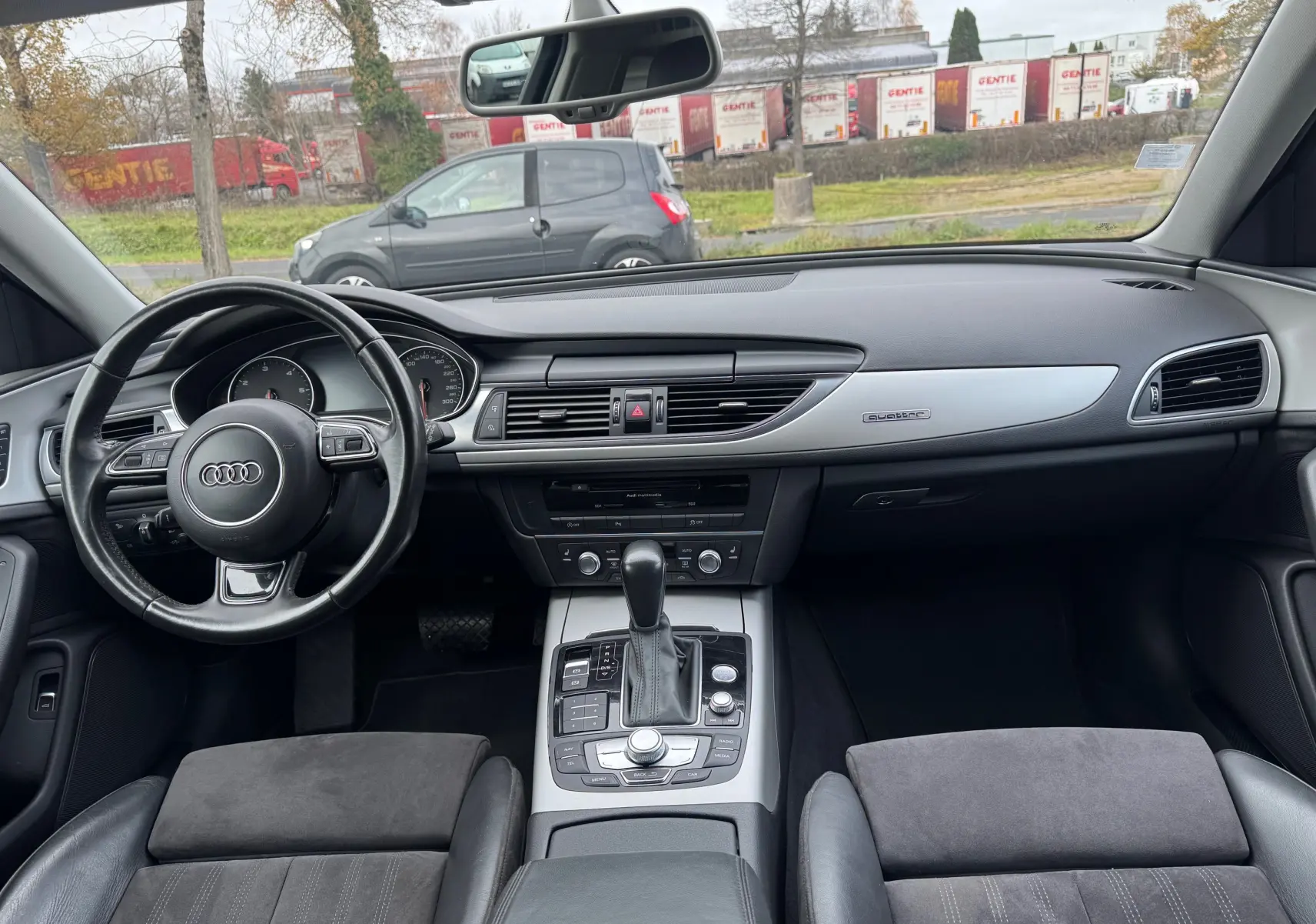 Vue intérieure avant de l’Audi A6 Avant 2015 noire, tableau de bord moderne avec console centrale et volant cuir multifonction.