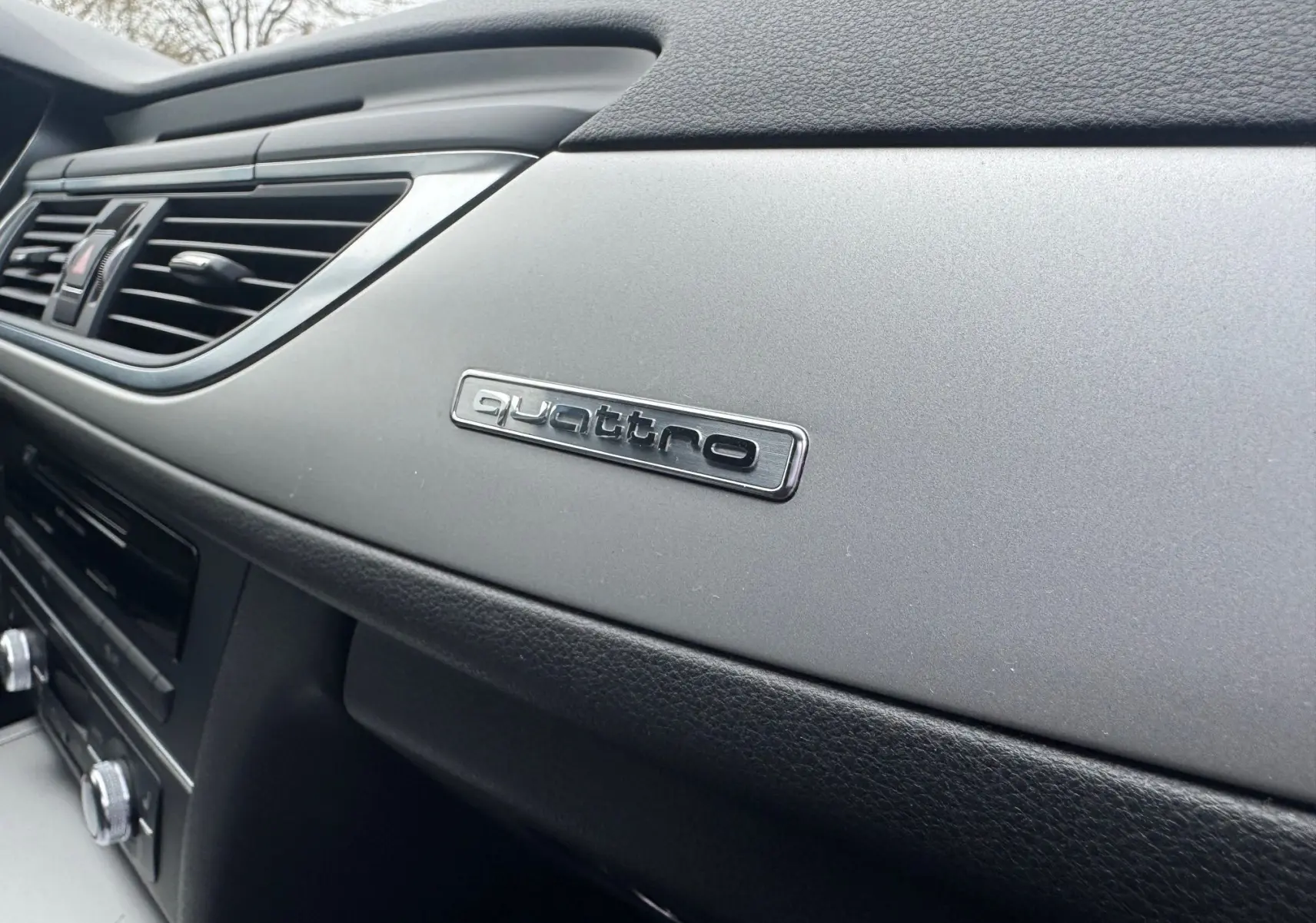 Détail intérieur du tableau de bord gris et noir de l’Audi A6 Avant 2015 avec logo quattro visible.