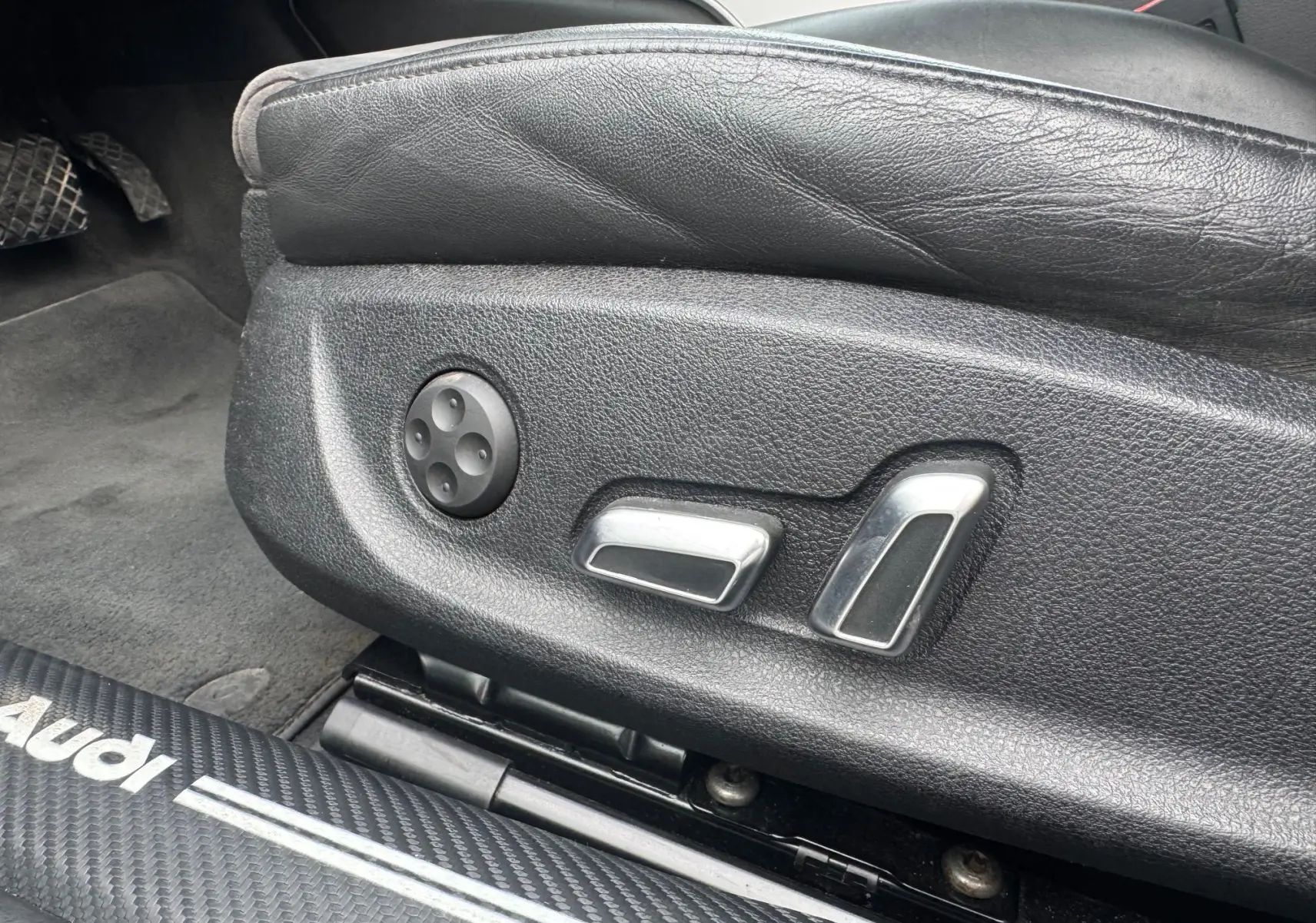 Gros plan sur les commandes de réglage électrique du siège conducteur en cuir noir d’une Audi A6 Avant 2015.