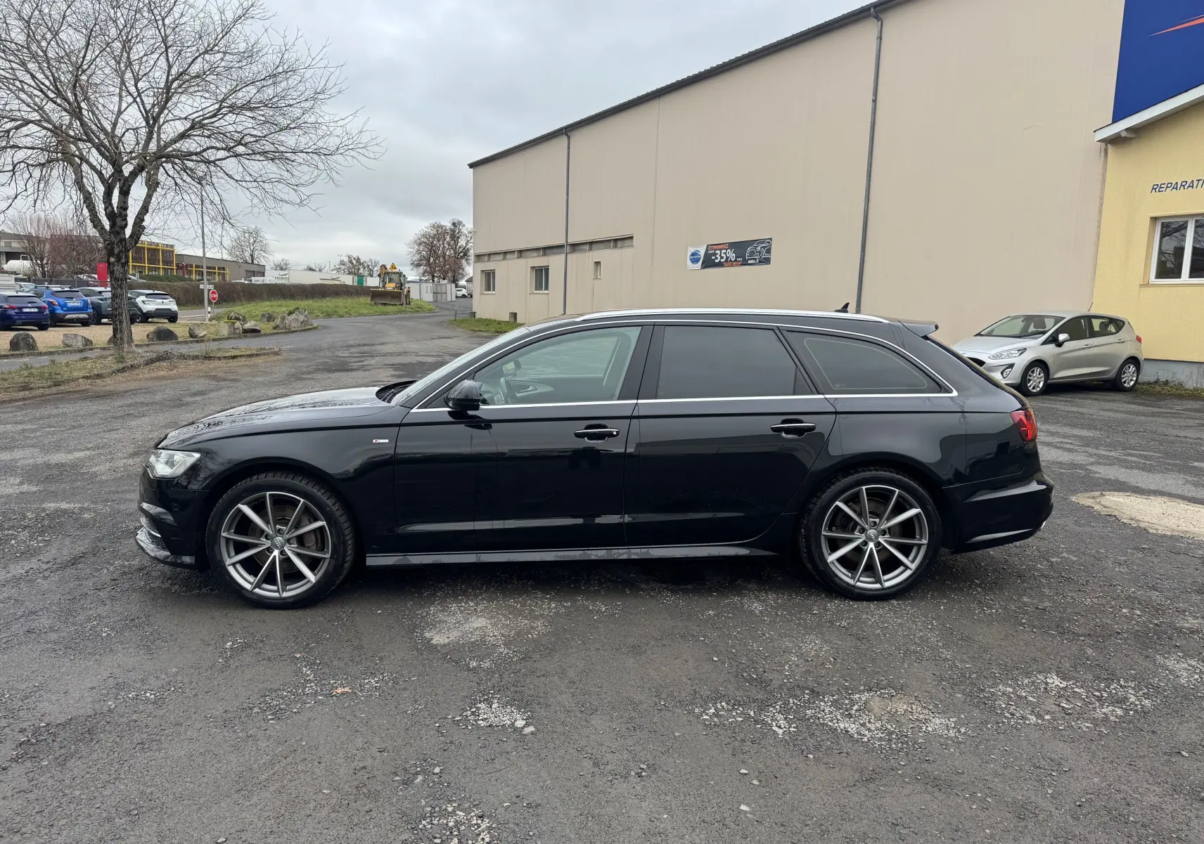 Audi A6 Avant noire vue de profil côté gauche, avec jantes alliage 19 pouces et vitres teintées.