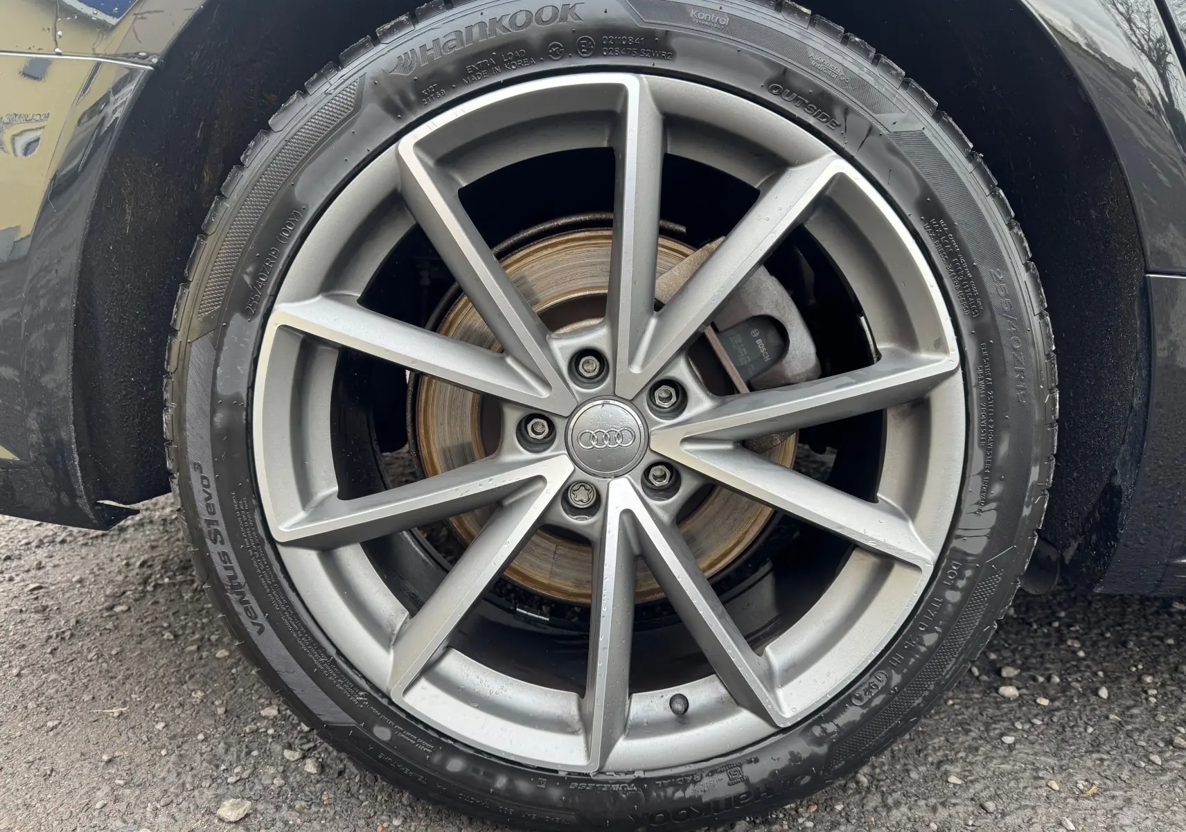 Gros plan sur la roue avant droite d’une Audi A6 Avant noire de 2015 avec jante alliage 19 pouces et logo Audi central.