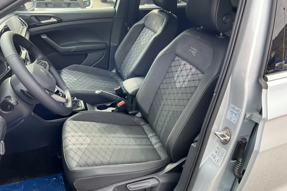 Vue intérieure côté conducteur du Volkswagen T-cross gris argent 2025, sièges tissu avec surpiqûres et logo R brodé.