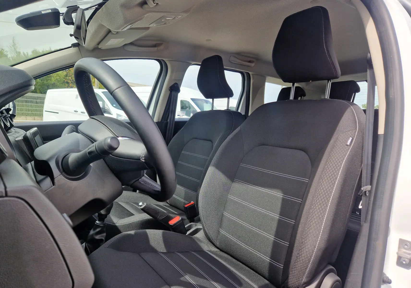 Vue intérieure côté conducteur du Dacia Duster blanc 2022, montrant les sièges noirs et le volant avec boîte manuelle.
