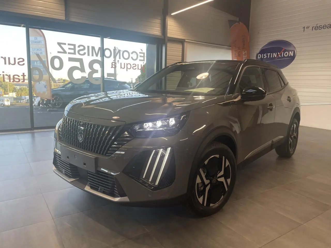 Peugeot 2008 gris métallisé en 3/4 avant droit, avec calandre noire et feux LED 3 griffes allumés en showroom.