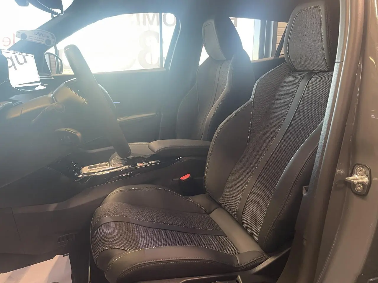 Vue intérieure côté conducteur du Peugeot 2008 gris, mettant en valeur les sièges sport en tissu et cuir avec surpiqûres contrastées.