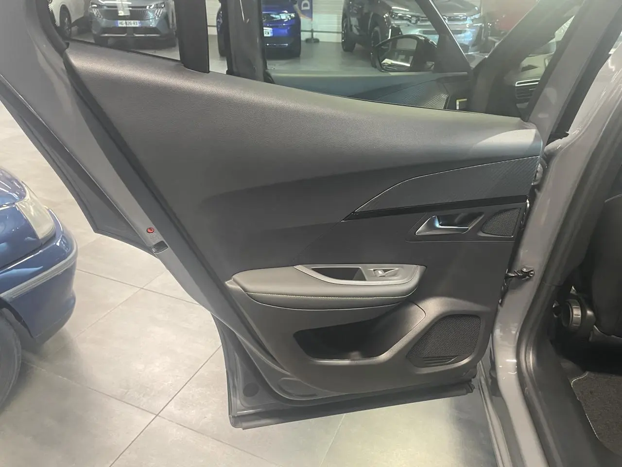 Porte arrière gauche ouverte du Peugeot 2008 gris, montrant le panneau intérieur noir avec accoudoir et haut-parleur intégré.